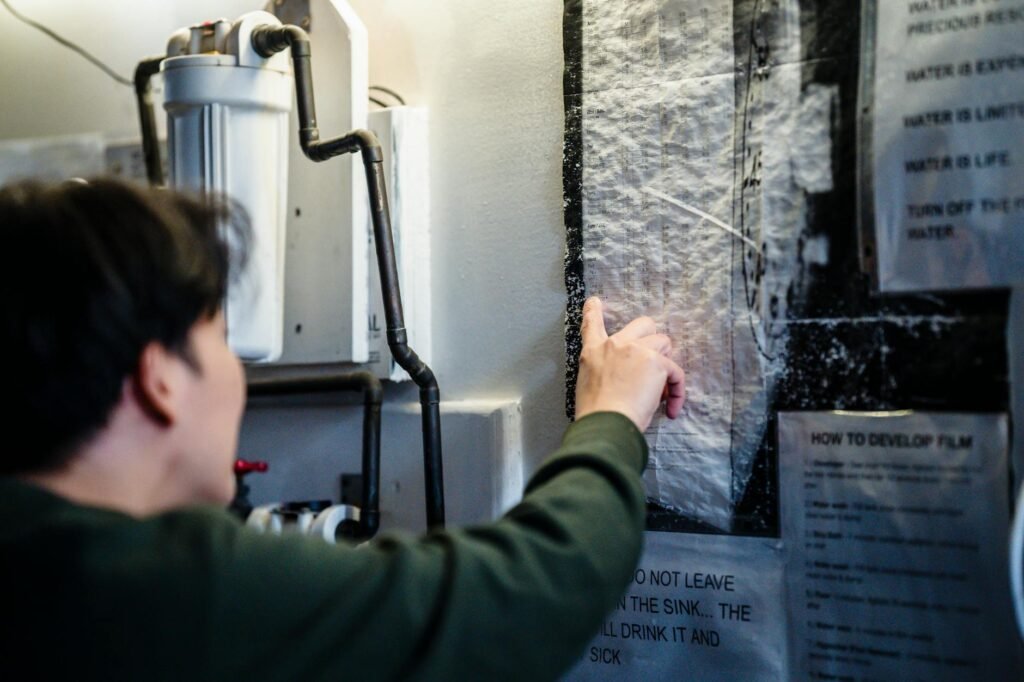 A homeowner inspecting a residential water heater in a utility area with a flashlight and notes.