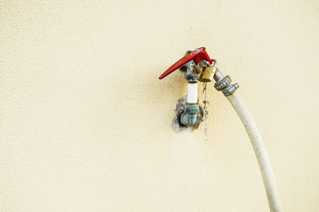 An outdoor faucet on a house wall with no hose attached and a foam cover ready to install.